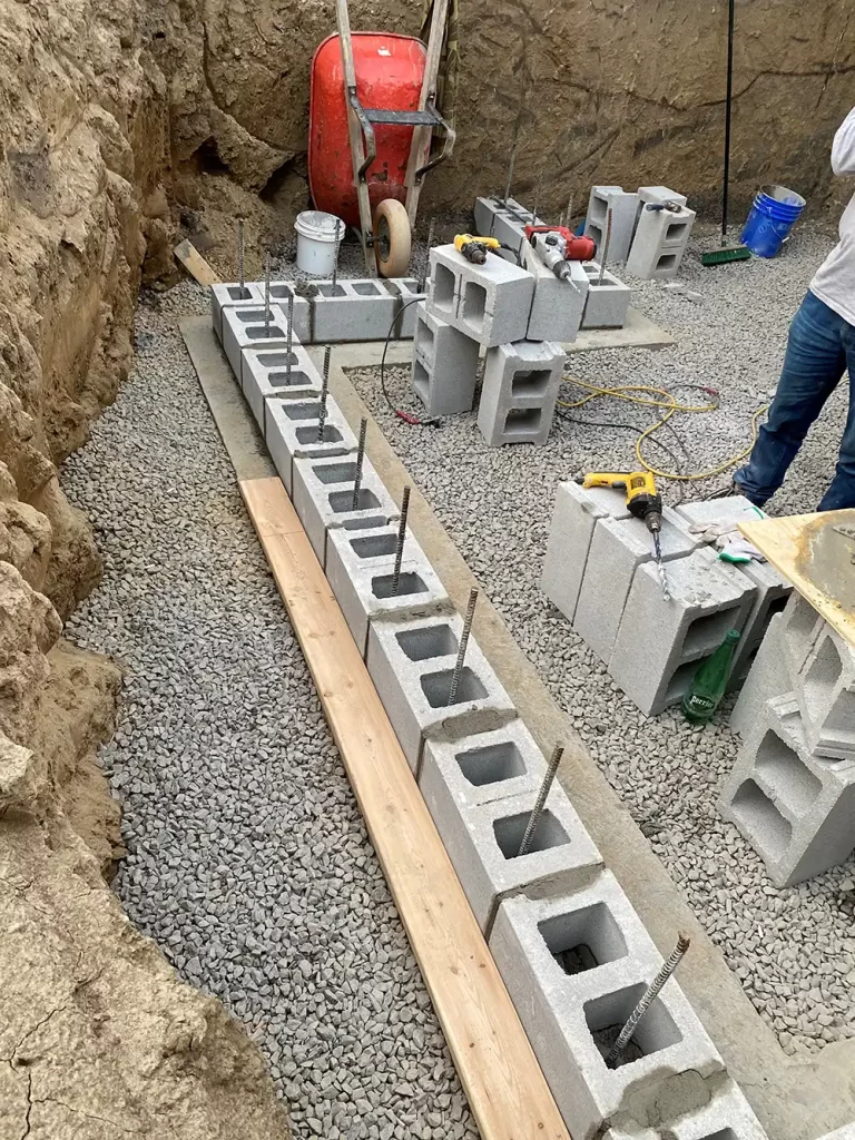 Laying the Bedrock: Constructing a New Foundation An active construction site with concrete blocks laid out over gravel for a new foundation, with construction tools and a worker present