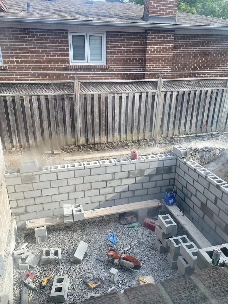 Erecting New Walls: The Rise of a Home Addition View of a construction site against a residential brick house, with new cinder block walls and scattered building tools