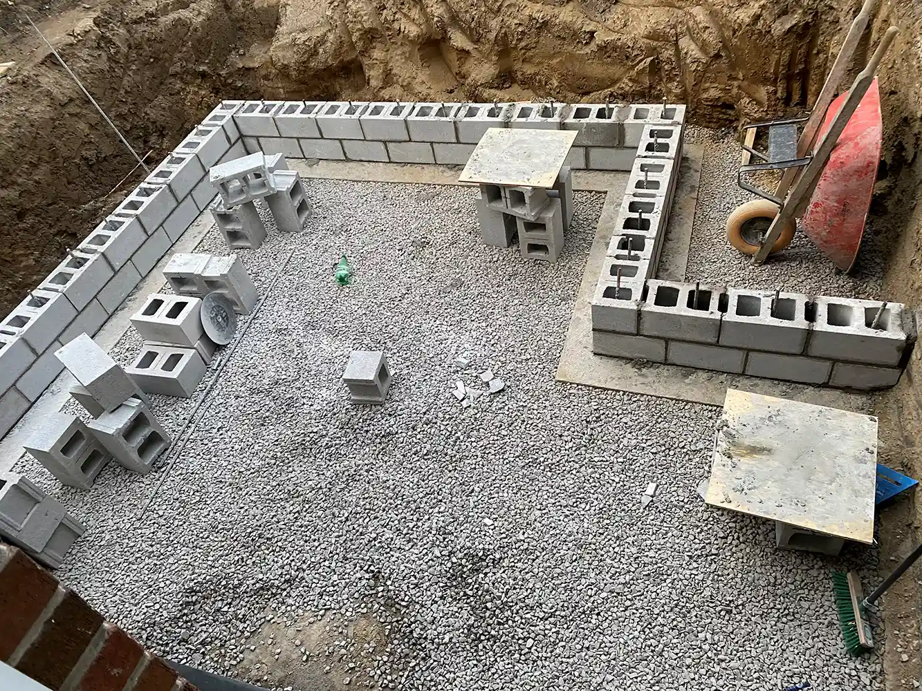 Overhead view of a construction site with cinder block walls being laid on a gravel foundation, surrounded by construction tools