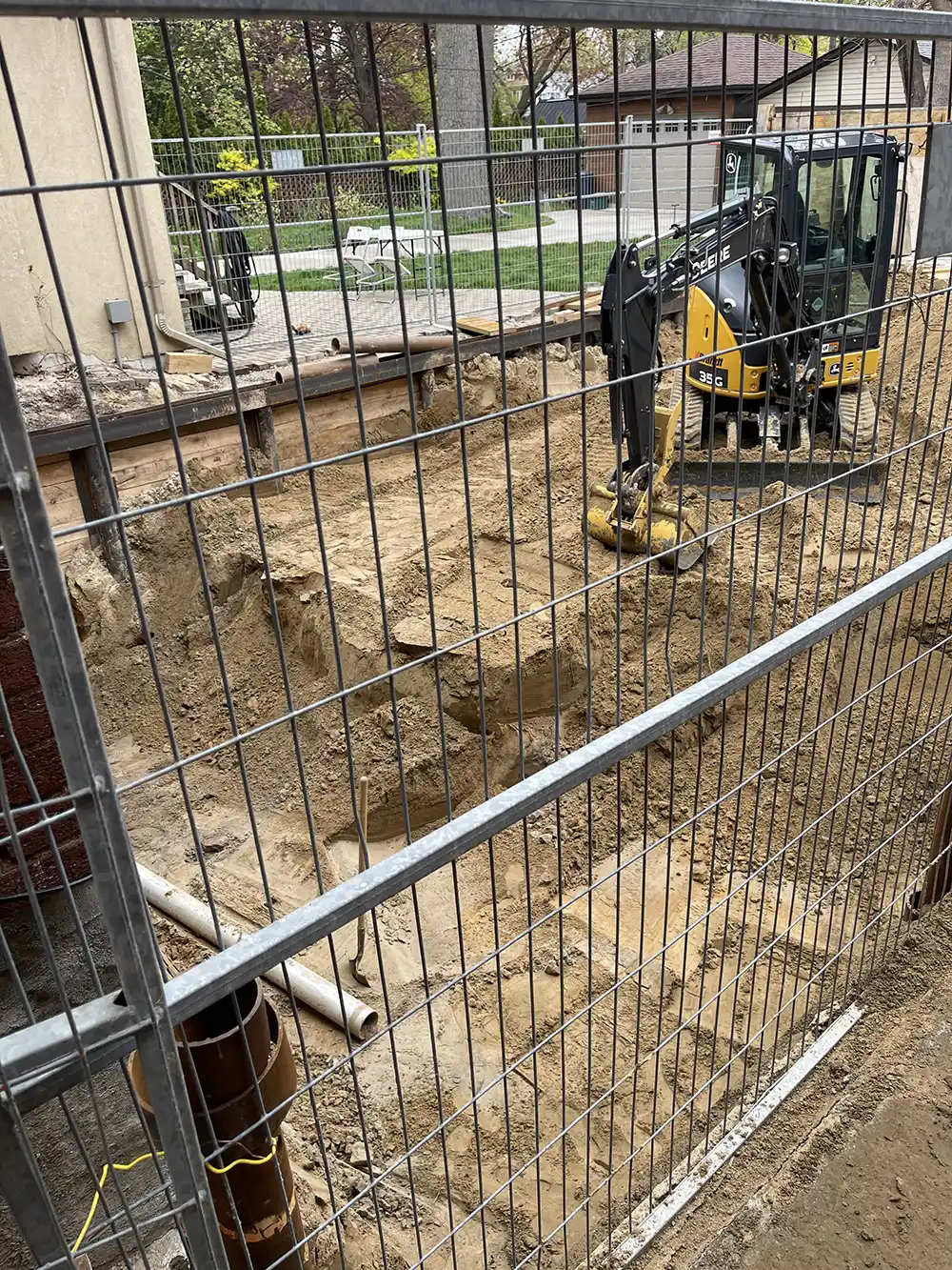 A construction site with an excavator at work behind a security fence, digging into the earth for new development.
