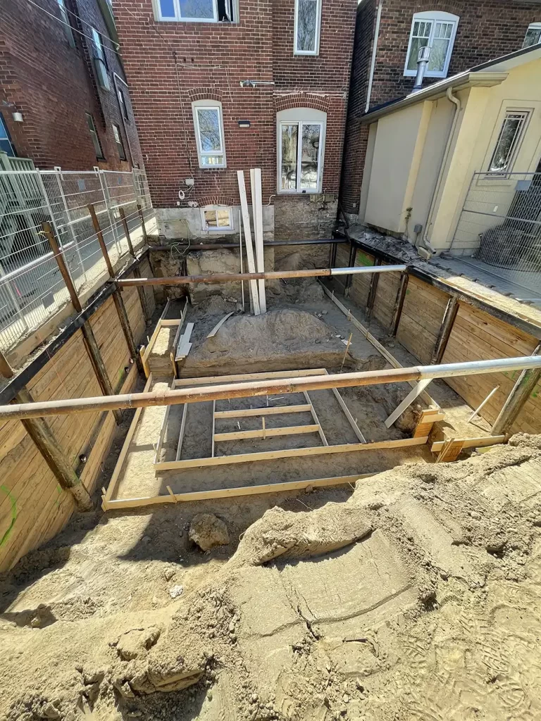 Architectural Excavation: Crafting a Foundation Deep excavation pit with wooden shoring on a residential property, prepped for foundation work under a clear sky