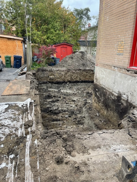 Excavation Site Preparation for Home Expansion An excavation site next to a brick building, with a deep trench dug out for the beginnings of a home expansion project