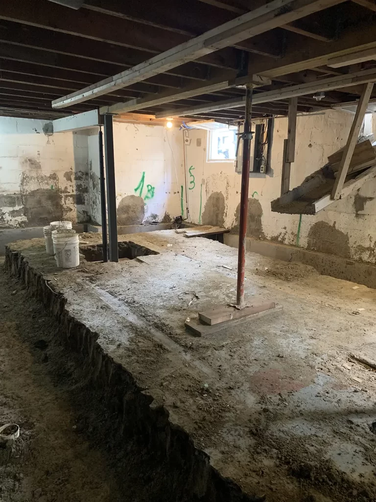 Reinforcing the Core: Basement Structural Work A basement undergoing structural enhancements with a perimeter trench, temporary support columns, and work lighting