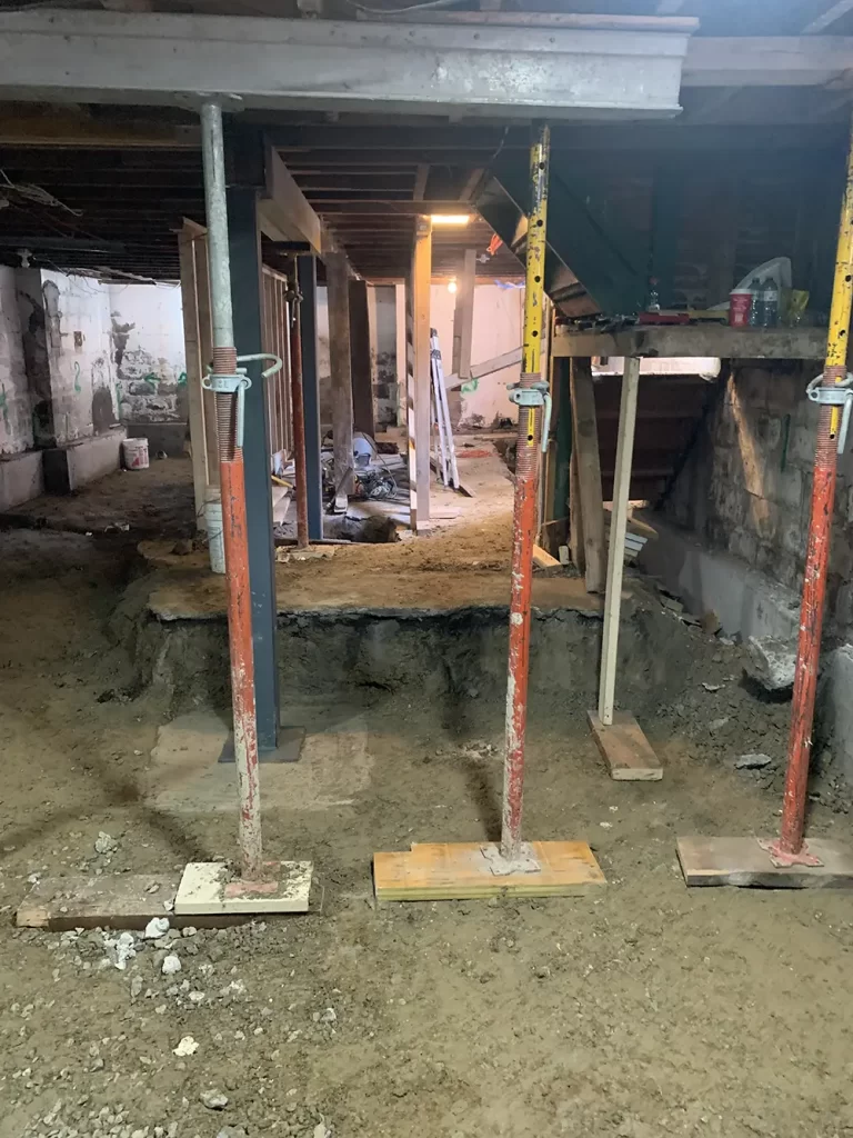 Underpinning in Action: Securing the Foundation Basement with metal shoring posts and exposed earth, illustrating the underpinning process for structural reinforcement.