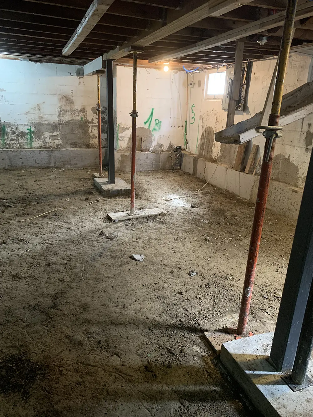A partially cleared basement with metal support beams and exposed floor joists, ready for structural improvements