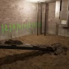 A basement with an exposed earthen trench where the concrete floor has been demolished, metal beams across the opening, and numbered sections on the walls, signifying the demolition stage in the underpinning process.