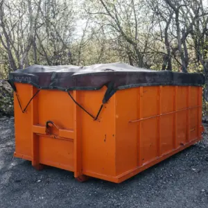 Bright orange 18-yard bin covered with a black tarp, situated on a gravel surface with a backdrop of budding trees.