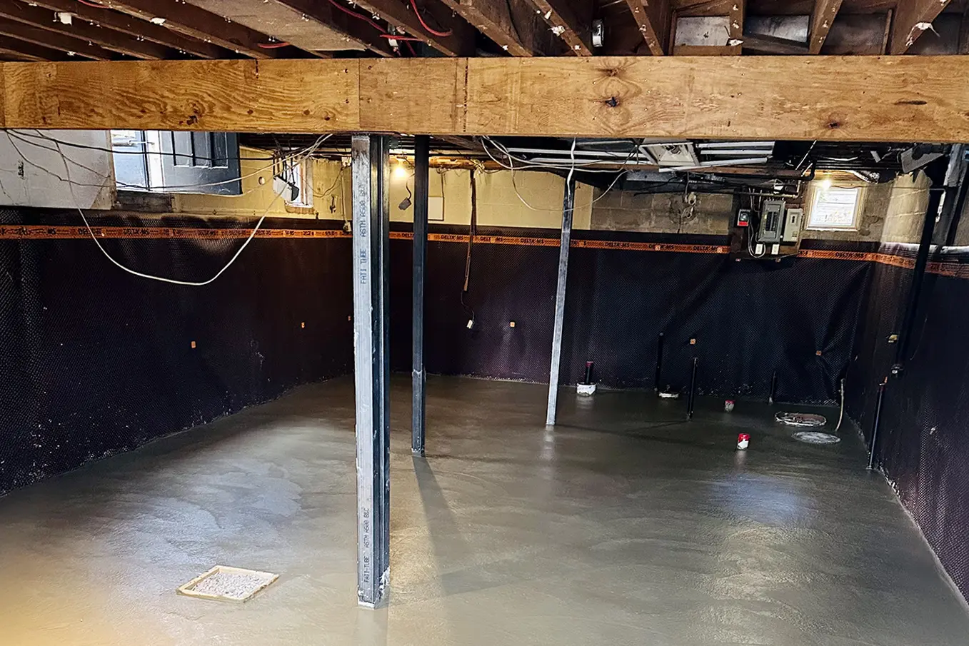 Freshly poured concrete floor in a basement lowering project with visible support beams and waterproofing membrane.