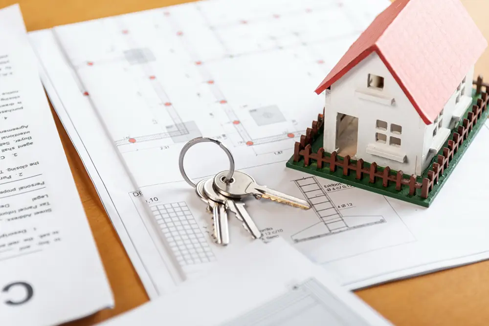 Model house and keys on top of building permit documents and blueprints