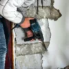 Construction worker using power tool to break foundation wall