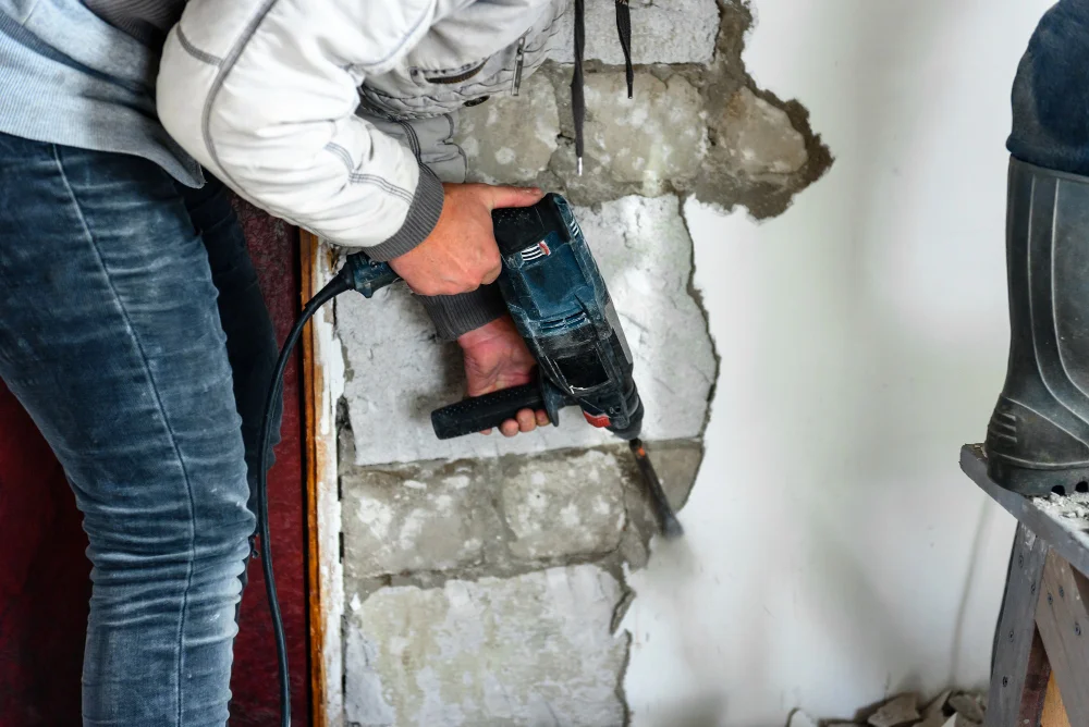 Construction worker using power tool to break foundation wall