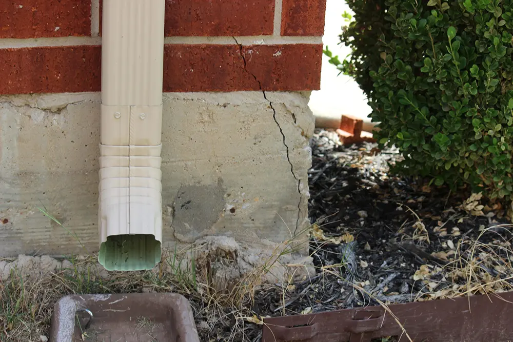 Visible vertical crack in concrete foundation beneath gutter spout