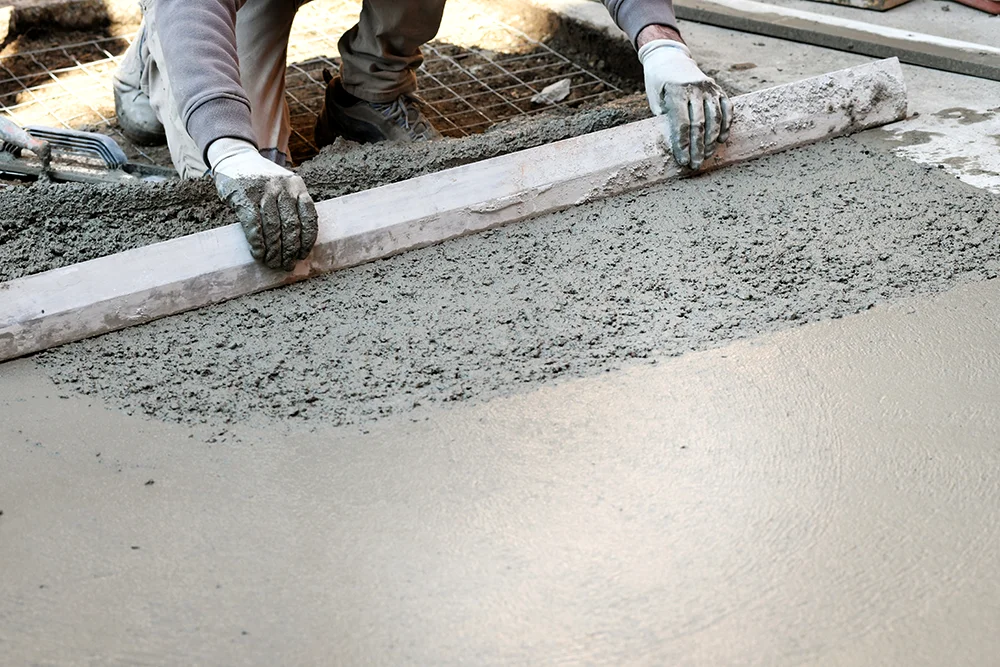 Worker smoothing freshly poured concrete with a screed tool